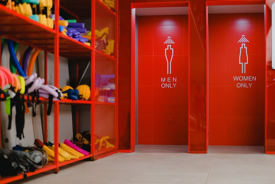 Colorful pool gear in storage beside gender-specific showers with vibrant red decor.